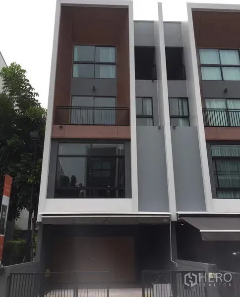 Townhouse for rent in Suan Luang, Bangkok - Modern multi-level townhouse facade with balconies and a covered carport in a landscaped community.