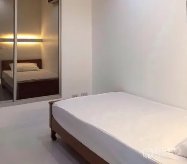 Condominium for rent in Bang Rak, Bangkok - Second bedroom with minimalist decor and a sliding mirrored door reflecting the bed.