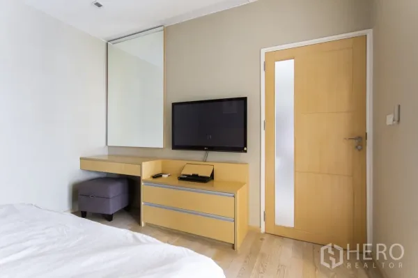 公寓 出租在Khlong Toei, Bangkok - 卧室角落设壁挂电视、内置斗柜、大镜面与浅木门。