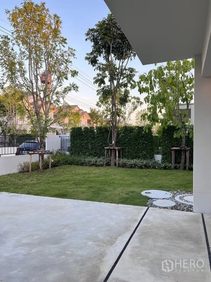 Detached House for rent in Bang Phli, Samut Prakan - Private garden with green lawn, young trees and a paved driveway behind the fence.