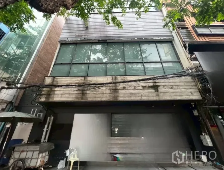 อาคารพาณิชย์ ให้เช่าในBang Rak, Bangkok - หน้าตึกช้อปเฮาส์กระจกบานกว้างพร้อมแผงโลหะใต้ร่มไม้