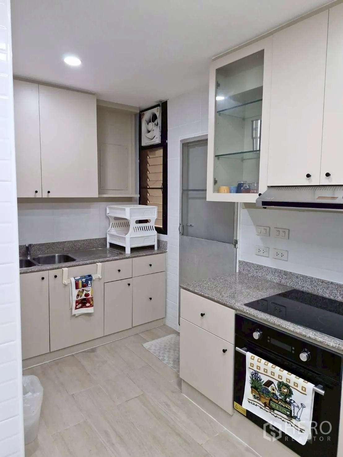 Condominium for rent in Khlong Toei, Bangkok - Kitchen from another angle with glass-front cabinet and door to utility zone.