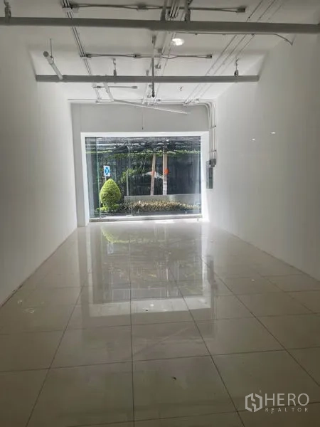 零售空间 出租在Khlong Toei, Bangkok - 明亮白盒子室内，瓷砖地面、挑高天花和轨道灯，面向大窗采光充足。