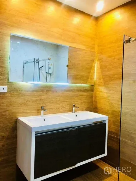 Home Office for rent or sale in Pak Kret, Nonthaburi - Contemporary bathroom with double vanity, backlit mirror and warm wood-tone walls.