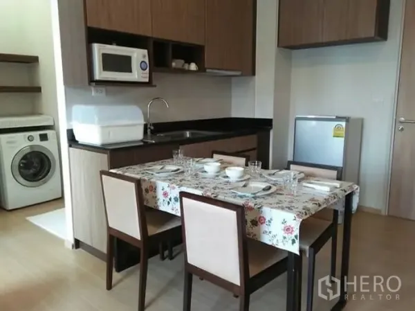 Condominium for rent in Huai Khwang, Bangkok - Compact kitchen and dining area with wood cabinetry, microwave, fridge and washing machine in a Bangkok condo.