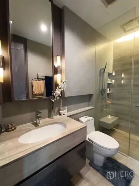 公寓 出租或出售在Bang Rak, Bangkok - 现代卫浴，带大理石台盆、马桶与玻璃淋浴间，灯光温暖。