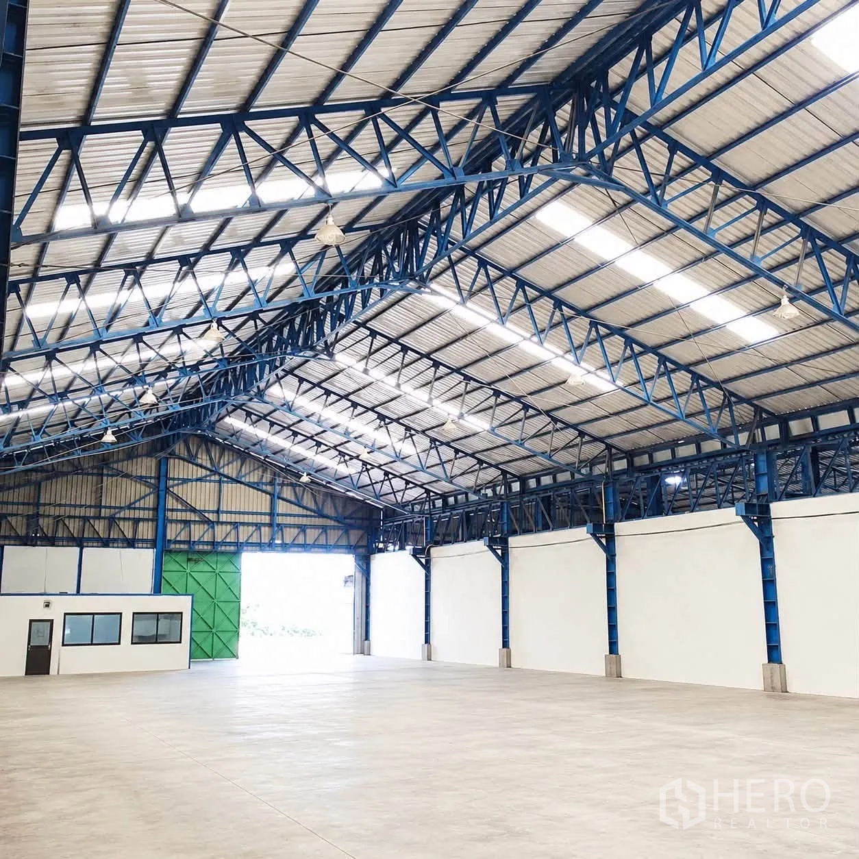 Warehouse for rent or sale - Open warehouse interior with steel truss roof, concrete floor, and a small office room near the entrance.