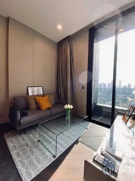 Condominium for rent in Khlong Toei, Bangkok - Sunny lounge with sofa, area rug, glass table, and floor-to-ceiling window with skyline view.