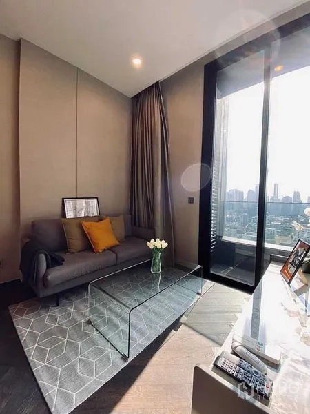 Condominium for rent in Khlong Toei, Bangkok - Sunny lounge with sofa, area rug, glass table, and floor-to-ceiling window with skyline view.