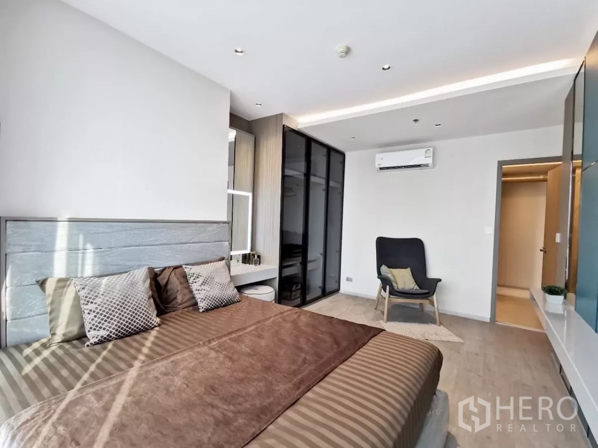 Condominium for rent in Watthana, Bangkok - Spacious master bedroom featuring glass wardrobe, accent chair and air conditioning.
