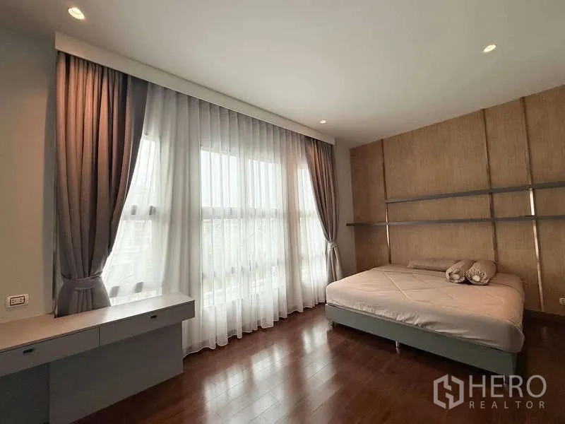 Detached House for rent or sale in Bang Phli, Samut Prakan - Bright guest bedroom with floor‑to‑ceiling curtains, large windows, built‑in desk and wood floors.