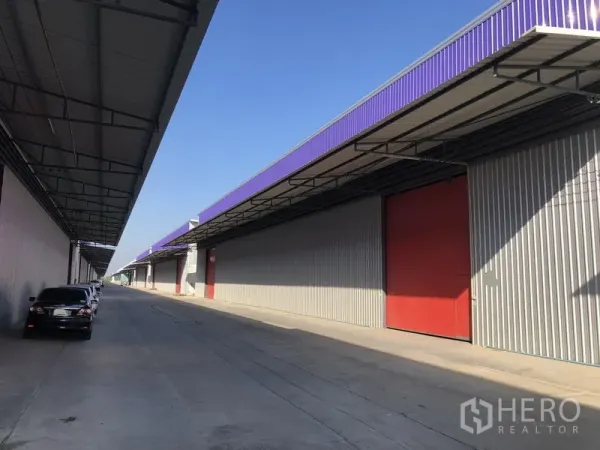 货栈 出租在Pathum Thani - 现代仓库一排，紫色檐口与大型红色推拉门，临宽阔通道。