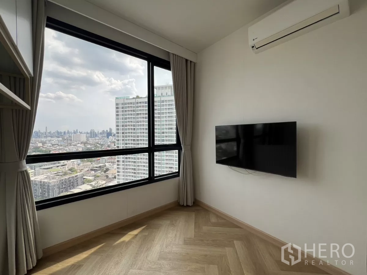 Condominium for rent or sale in Chatuchak, Bangkok - Second bedroom with wall‑mounted TV, air‑conditioner and expansive city‑view window.