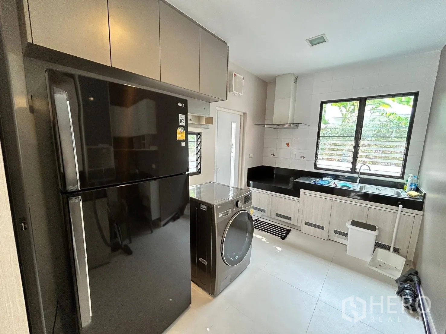 Detached House for rent or sale in Prawet, Bangkok - Modern kitchen with black refrigerator, front-load washer, L-shaped counters, range hood, sink and window.