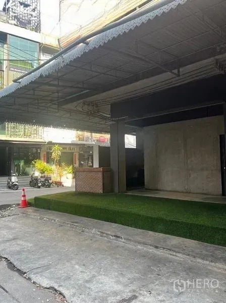 零售空间 出租在Watthana, Bangkok - 街景视角的店面外立面，深挑雨棚与人造草坪坡道