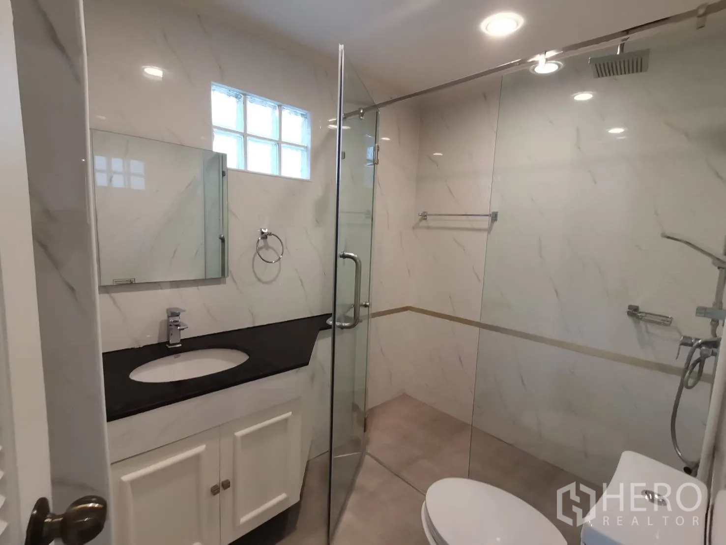 Condominium for rent in Watthana, Bangkok - Bathroom with marble-look walls, glass shower enclosure, and vanity sink.