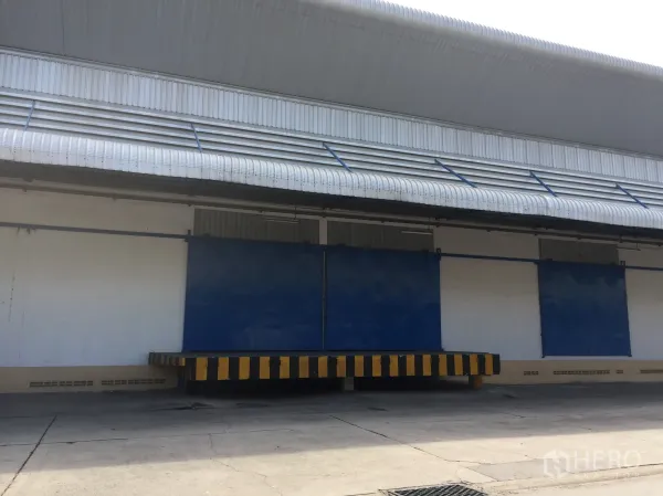 货栈 出租在Lat Krabang, Bangkok - 带雨棚的装卸月台与蓝色推拉门，外墙设通风百叶的仓库外观