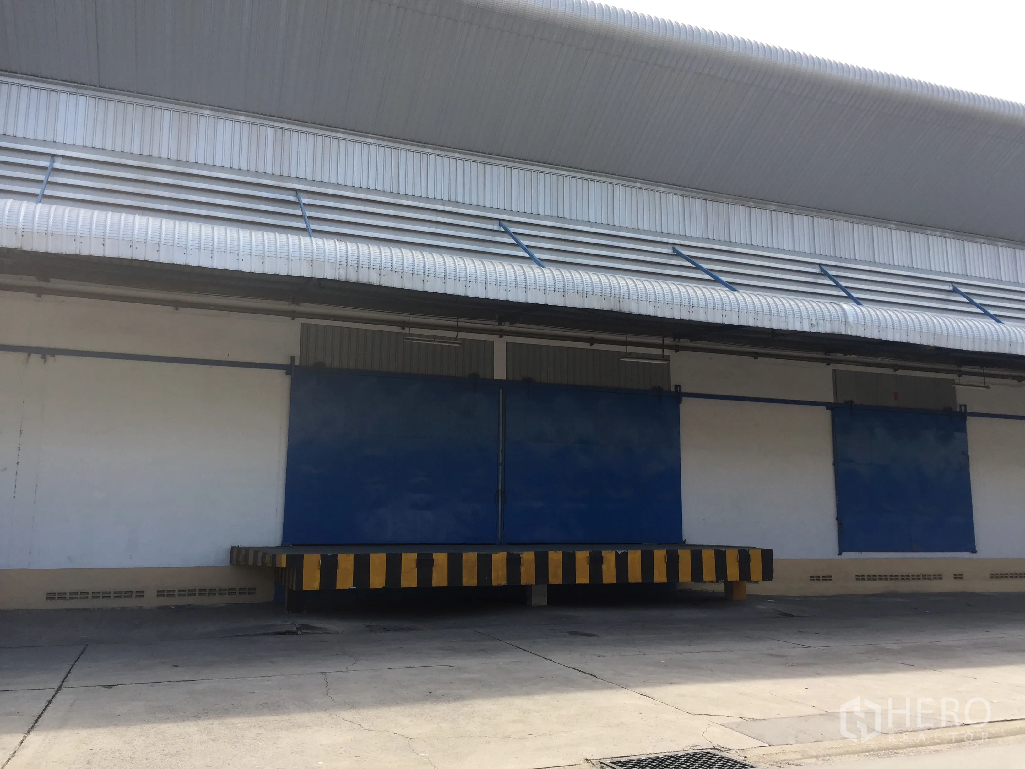 货栈 出租在Lat Krabang, Bangkok - 带雨棚的装卸月台与蓝色推拉门，外墙设通风百叶的仓库外观