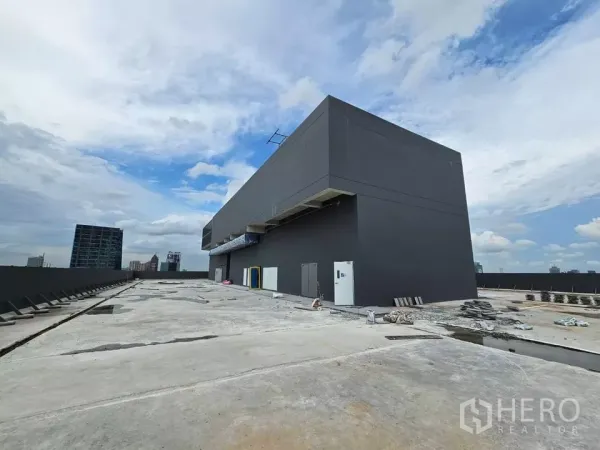 零售空间 出租 - 宽阔混凝土屋顶，深灰机房与曼谷天际线在蓝天下。