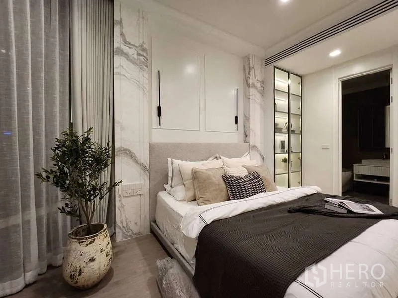Condominium for sale in Watthana, Bangkok - Primary bedroom with upholstered bed, marble feature wall and illuminated glass display cabinet.