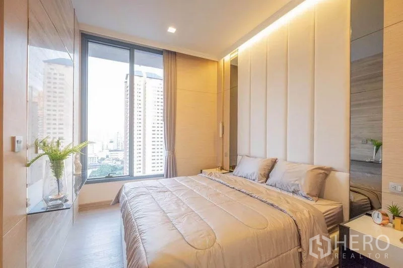 Condominium for rent in Watthana, Bangkok - Cozy bedroom with large window and city view, padded headboard and built-in shelving.