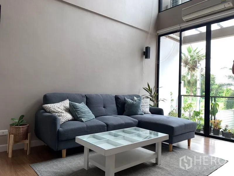 ทาวน์เฮาส์ ให้เช่าในKhlong Toei, Bangkok - ห้องนั่งเล่นอบอุ่น โซฟาเข้ามุม โต๊ะกลางกระจก และประตูกระจกบานใหญ่สู่ระเบียง