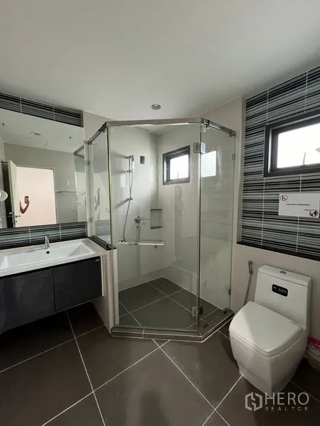 Detached House for rent in Bang Kapi, Bangkok - Bathroom with corner glass shower, vanity and striped tile accent.