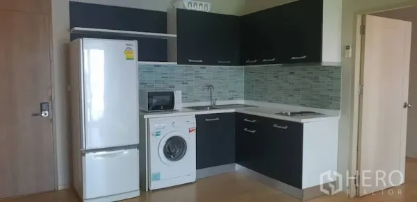 Condominium for rent in Watthana, Bangkok - Compact kitchen with black-and-white cabinets, tiled backsplash, fridge, washing machine, microwave and sink.