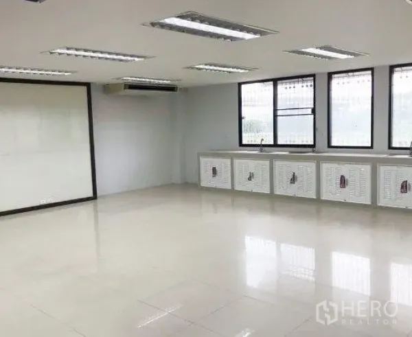 Office Space for rent or sale in Don Mueang, Bangkok - Bright open-plan office with light tile floors, large windows, built-in cabinets with sink, ceiling fluorescent lights and wall AC.
