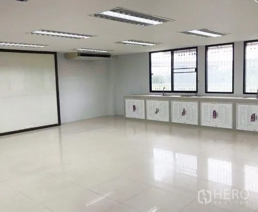 Office Space for rent or sale in Don Mueang, Bangkok - Bright open-plan office with light tile floors, large windows, built-in cabinets with sink, ceiling fluorescent lights and wall AC.