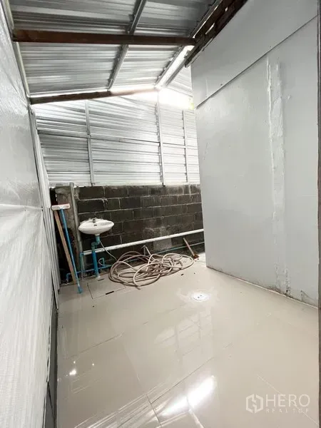 Warehouse for rent in Wang Thonglang, Bangkok - Utility area with sink and hose under a metal roof beside the main storage hall.