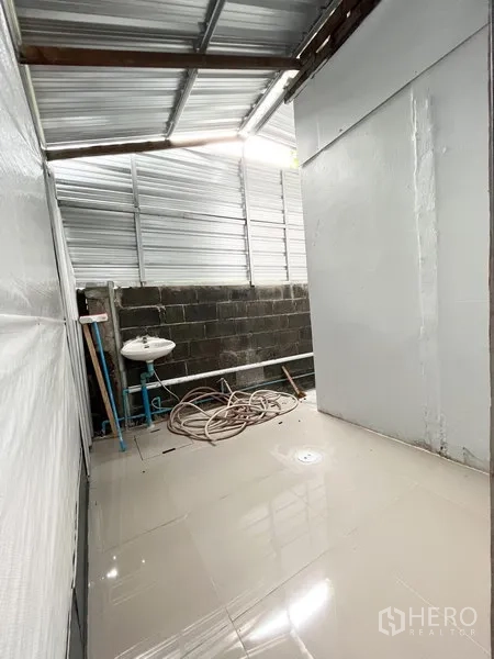 Warehouse for rent in Wang Thonglang, Bangkok - Utility area with sink and hose under a metal roof beside the main storage hall.