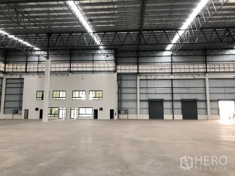Factory for rent in Samut Prakan - Wide‑span warehouse interior with multiple roller shutters, internal offices and tall insulated roof.