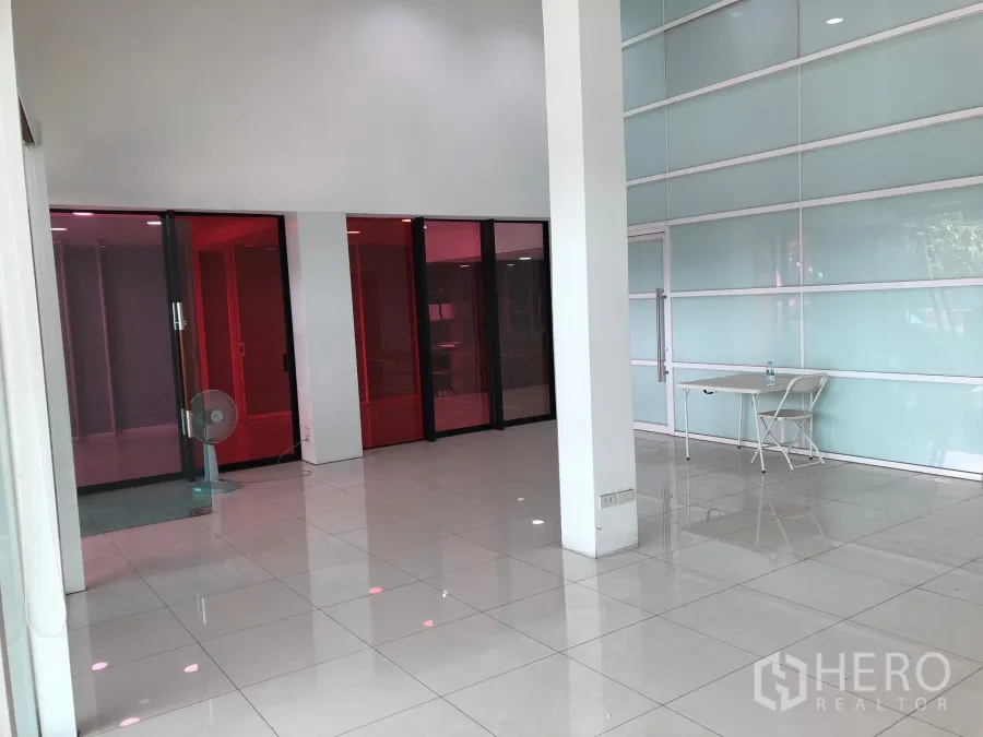 店屋 出租或出售在Khan Na Yao, Bangkok - 明亮的一层商铺空间，白色亮面地砖、挑高天花与红色玻璃隔间。