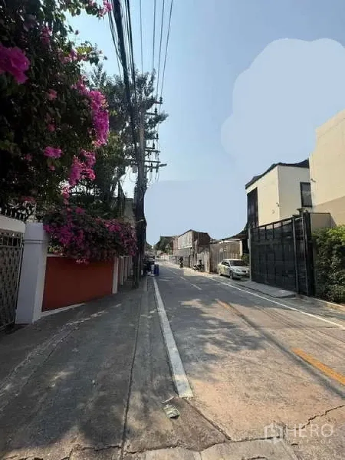 Land for sale in Khlong Toei, Bangkok - Quiet residential soi in Khlong Toei with bougainvillea, overhead cables, gated modern homes and a parked car on a sunny day.