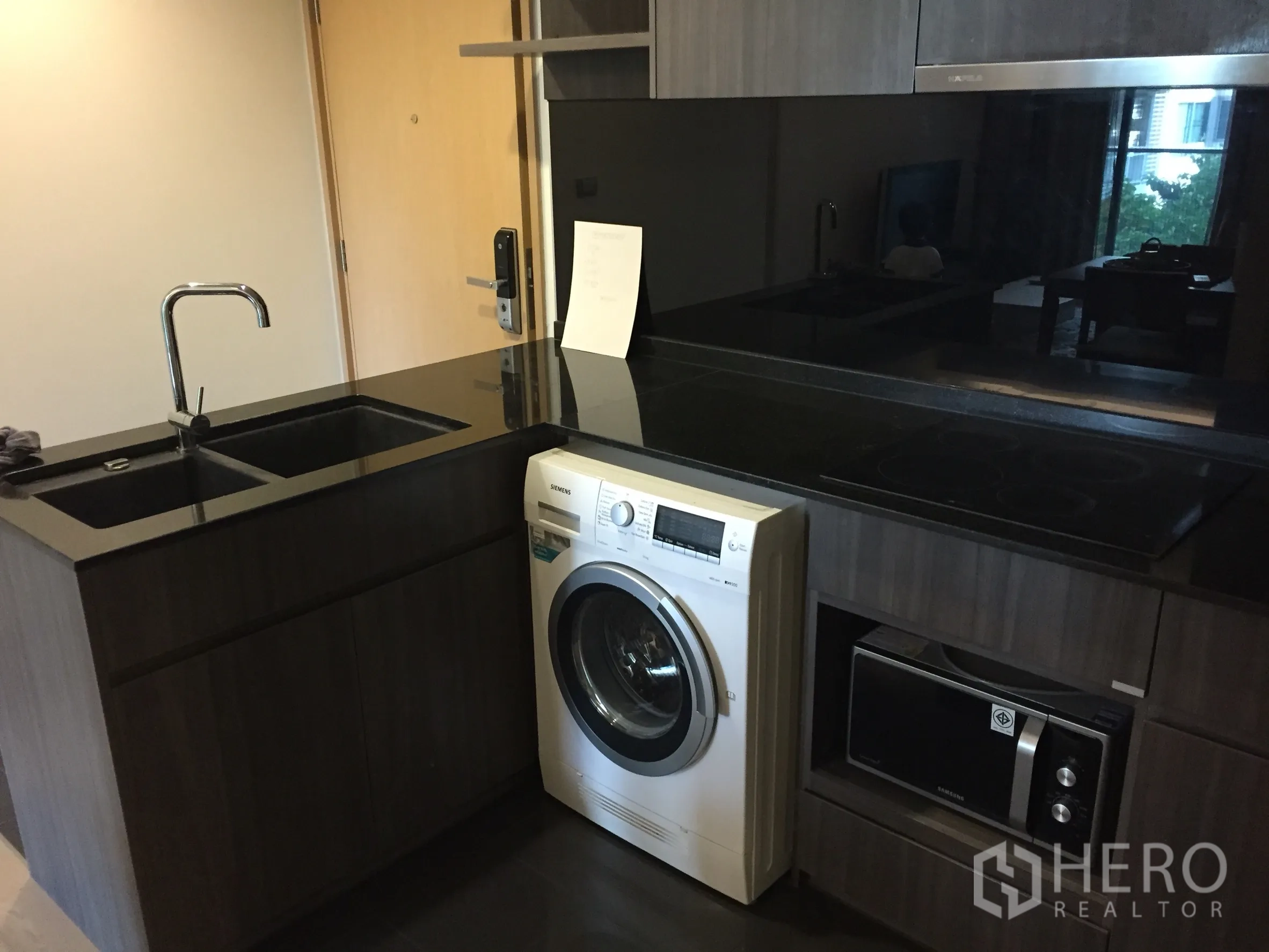 คอนโด ให้เช่าหรือขายในWatthana, Bangkok - ครัวบิวท์อินสไตล์โมเดิร์น เคาน์เตอร์หินแกรนิต อ่างล้างจานคู่ เตาไฟฟ้า เครื่องซักผ้า และไมโครเวฟในตู้ไม้สีเข้ม.