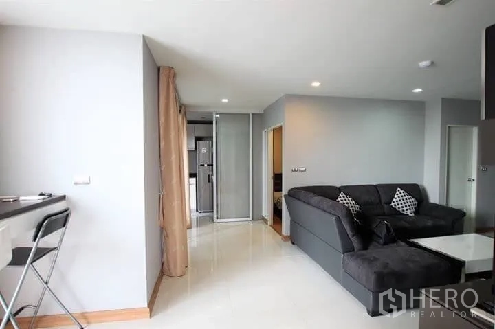 Condominium for rent in Watthana, Bangkok - Open-plan living area with L-shaped sofa, tiled floors and breakfast bar beside the kitchen.