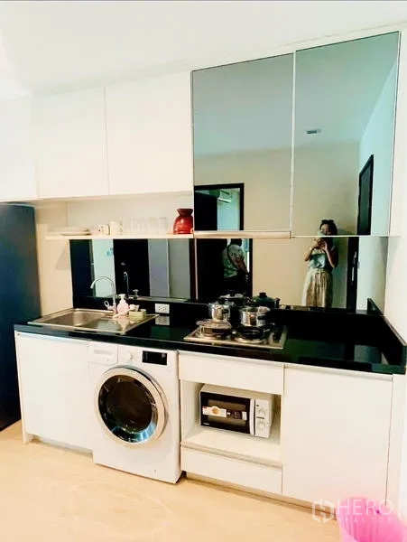 Condominium for rent - Compact white kitchenette with black countertop, sink, hob, microwave, and washing machine.