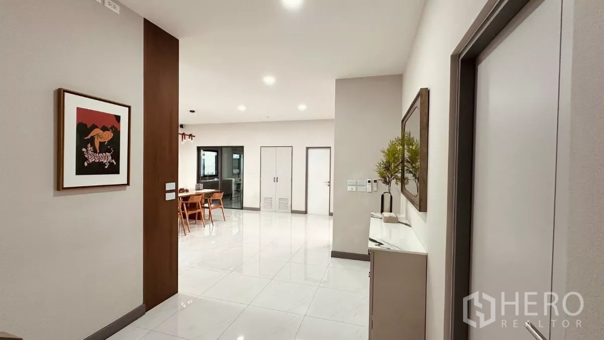 Detached House for rent in Bang Phli, Samut Prakan - Hallway with artwork and glossy floors leading to the dining and kitchen areas.