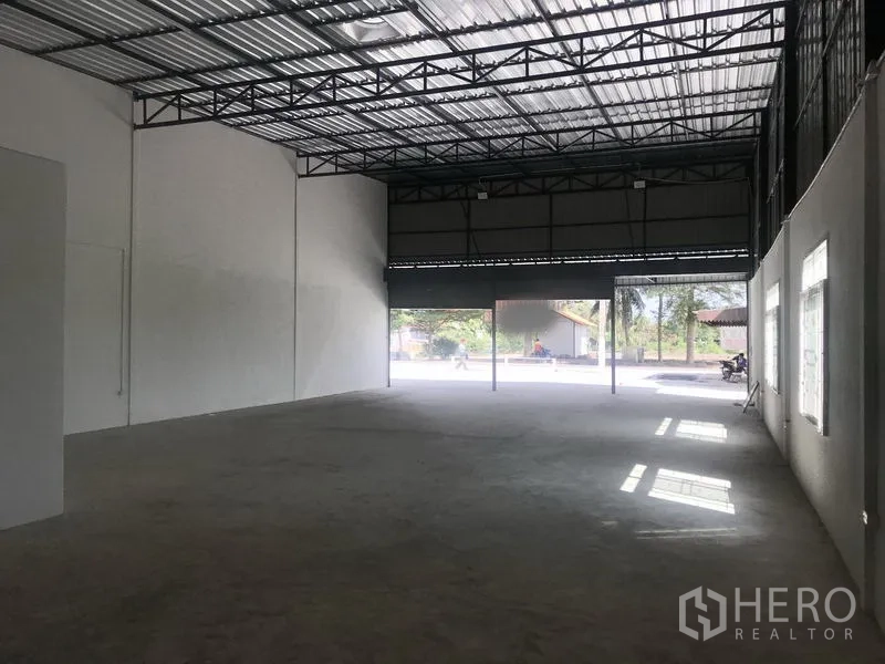Warehouse for rent in Lam Luk Ka, Pathum Thani - Spacious interior looking toward the entrance with two large roller shutters and natural light.