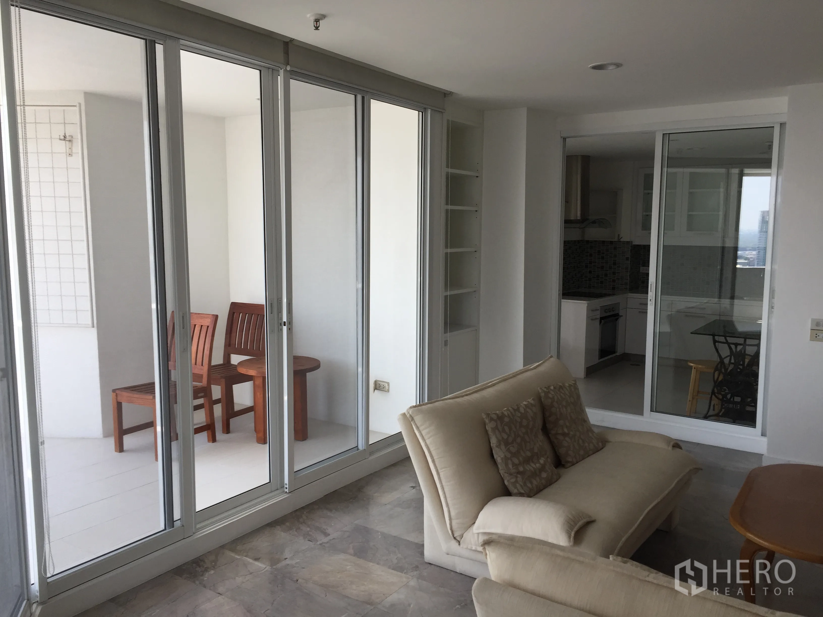 คอนโด ให้เช่าในWatthana, Bangkok - ห้องนั่งเล่นเปิดออกสู่ระเบียงกระจกพร้อมชุดที่นั่ง และครัวแยก