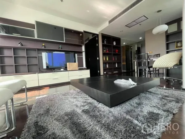 Condominium for rent or sale in Watthana, Bangkok - Living area with built-in media wall, square low coffee table on a shag rug, shelves and a dining nook.