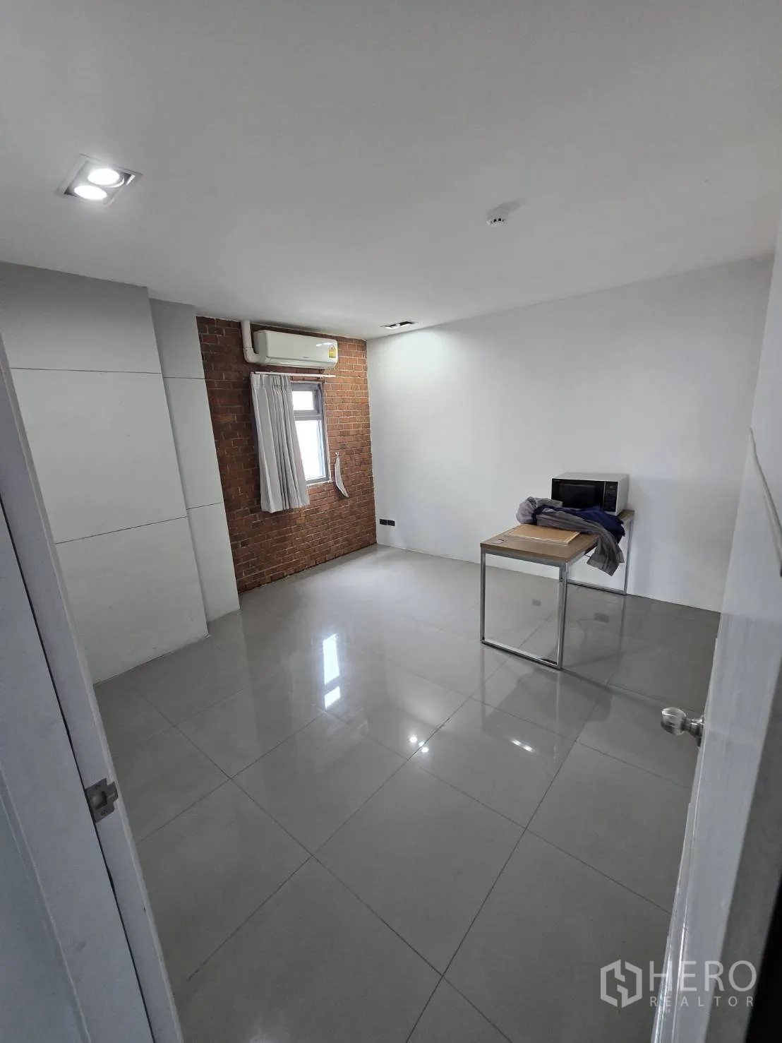Office Space for rent in Watthana, Bangkok - Bright room with window, air conditioner, brick accent wall, and tiled floors.