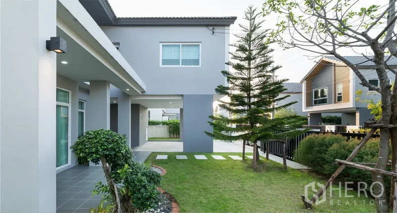 Detached House for sale in Lam Luk Ka, Pathum Thani - Private backyard with green lawn, pine tree, stepping stones and covered terrace.