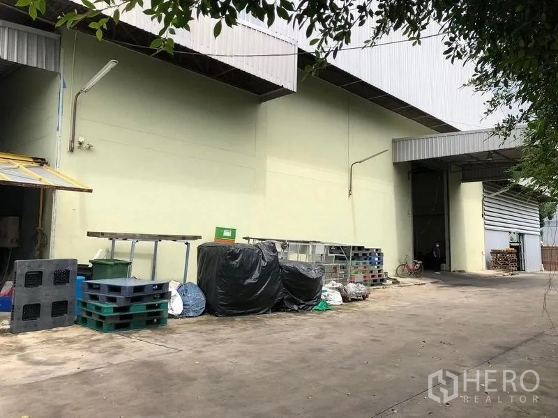 Factory for rent or sale in Khlong Luang, Pathum Thani - Factory exterior with covered loading bay, wide roller door and outdoor storage in Khlong Luang.