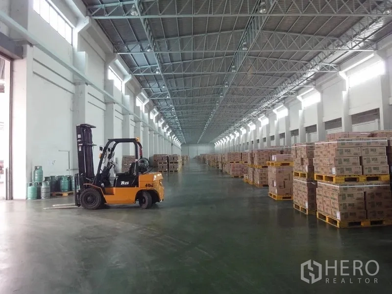 货栈 出租在Bang Sao Thong, Samut Prakan - 叉车在明亮的仓库通道作业，两侧为托盘货物。