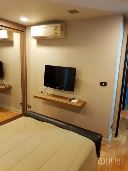 Condominium for sale in Bang Rak, Bangkok - Bedroom corner with mirror wardrobe, wall-mounted TV and air conditioner.