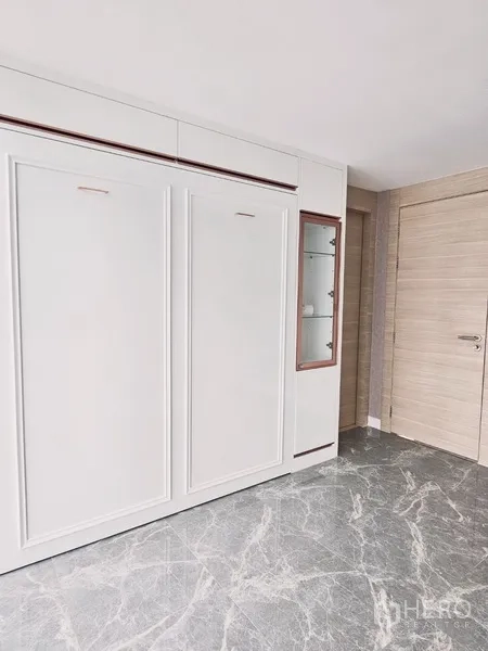 Condominium for sale in Bang Rak, Bangkok - Spare room with sleek white cabinetry and stone-look flooring beside a wooden door.