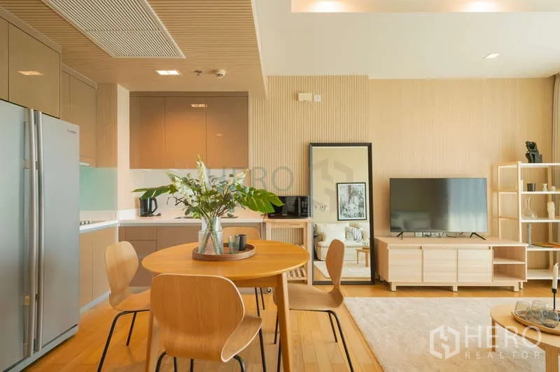 Condominium for sale in Khlong Toei, Bangkok - Open-plan kitchen and dining area with round wooden table, built-in cabinets, and a large refrigerator.