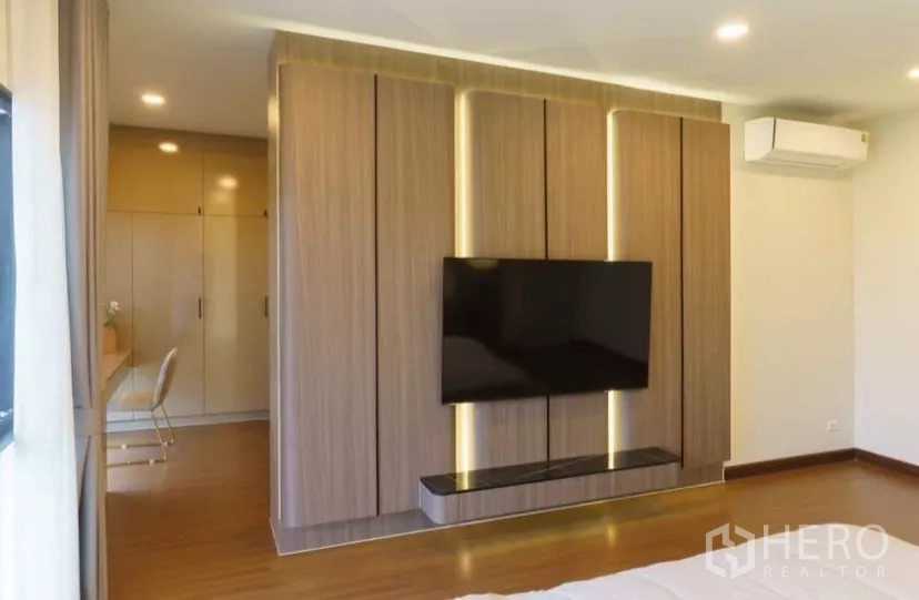 Detached House for rent or sale in Bang Phli, Samut Prakan - Bedroom with wood-panel TV wall, built-in wardrobe and study desk.